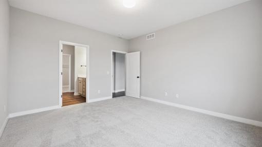 A large empty room with a carpeted floor and two doors.