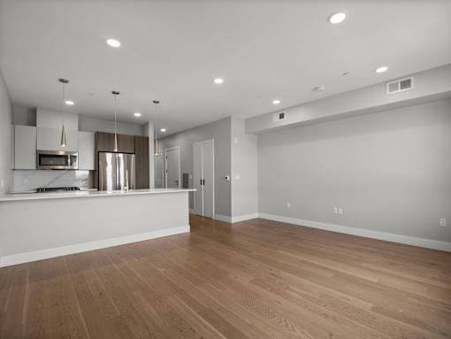 A spacious room with wooden flooring and a kitchen area with stainless steel appliances.
