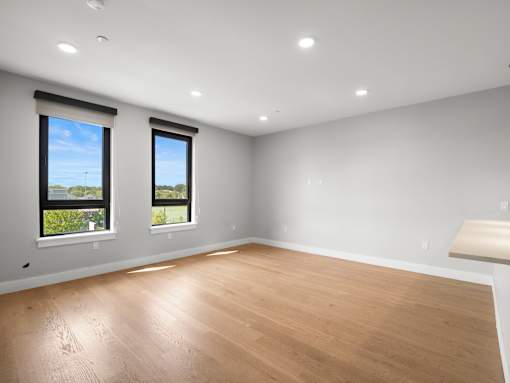 A room with wooden flooring and two windows.