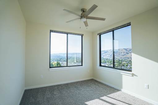 A room with a ceiling fan and two windows overlooking a cityscape.