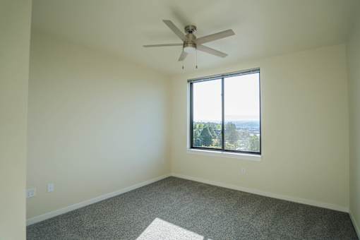 A room with a ceiling fan and a window overlooking a cityscape.