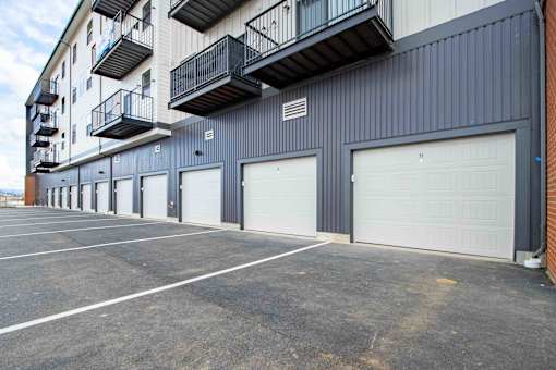 A parking lot in front of a grey building with a balcony on the second floor.