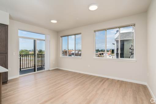 A large empty room with wooden floors and windows overlooking a fenced area.