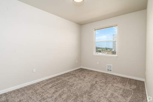 A room with a carpeted floor and a window showing a view of a cityscape.