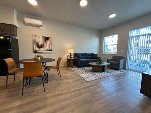 A living room with a grey couch, a black cabinet, a round table with four chairs, and a rug.