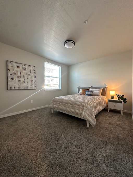 A bedroom with a bed, nightstand, and a window.
