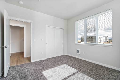 A room with a large rug in the middle and a window with blinds.