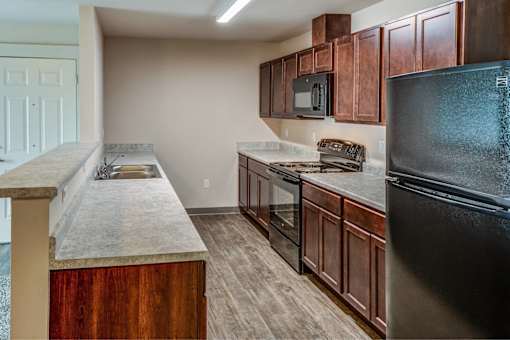 A kitchen with dark wood cabinets and a black refrigerator.