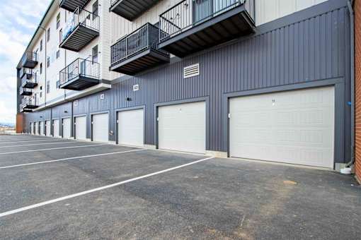 A parking lot in front of a grey building with a balcony on the second floor.