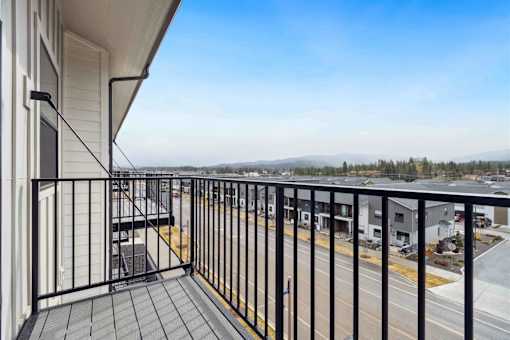 A balcony with a black railing and a view of a parking lot and distant trees.