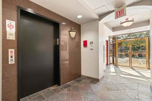 A hallway with a black door and a red fire alarm on the wall.