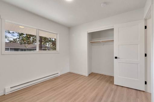 A room with a white door, a window, and a wooden floor.