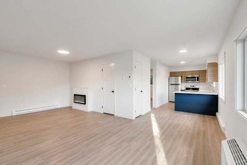 A spacious living room with a fireplace and a kitchen area in the background.