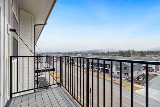 A balcony with a black railing and a view of a parking lot and trees.
