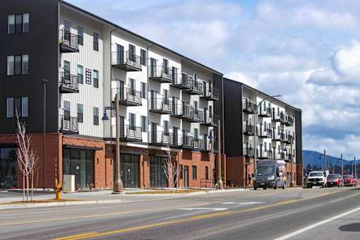 A modern apartment building with balconies and a parking lot in front.