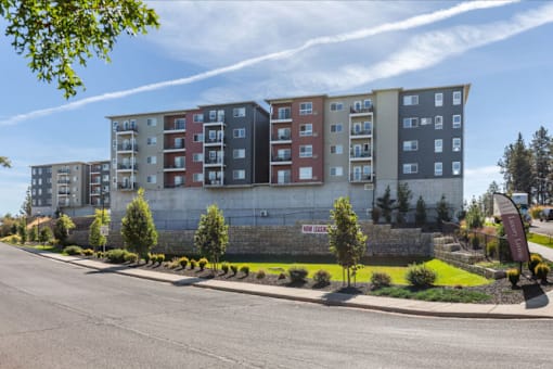 A row of multi-story apartment buildings with trees and shrubs in front.
