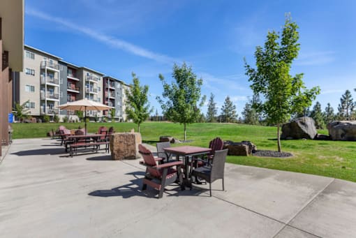 A patio with a table and chairs is surrounded by trees and apartment buildings.
