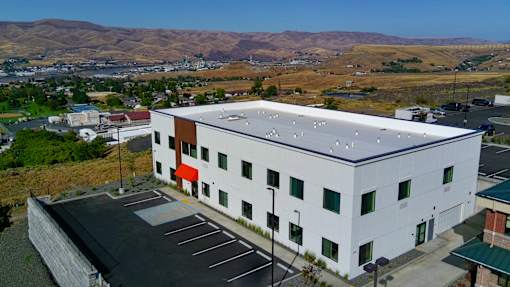A white building with a red awning is surrounded by a parking lot.