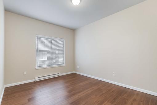 A room with wooden flooring and a window with blinds.
