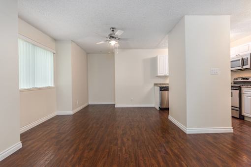 an empty living room with a ceiling fan and a kitchen in the background