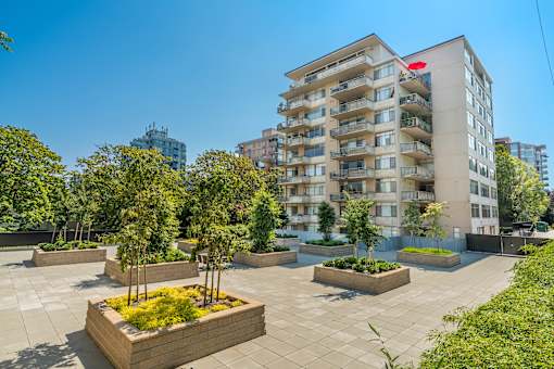 A modern apartment building with a courtyard garden in the foreground.