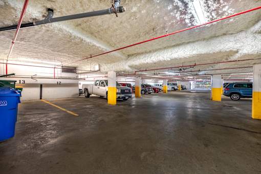 A parking garage with several cars parked and a blue trash can on the left.