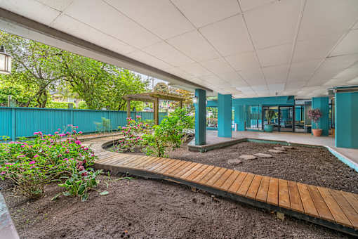 A garden with a wooden walkway and a green building in the background.