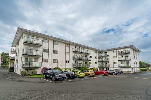 A large white apartment building with cars parked in front.