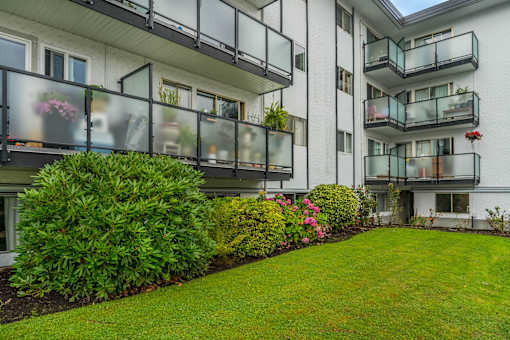 A white building with balconies and green bushes in front.