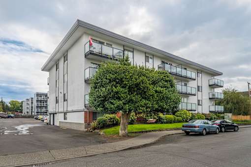 A white building with a red flag on the left side and cars parked in front.