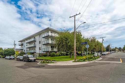 A street view of a residential area with apartment buildings and cars parked on the side of the road.