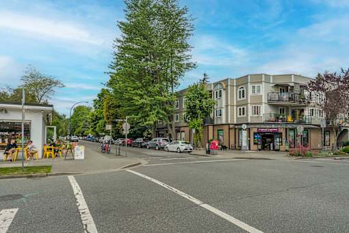 A street view of a residential area with apartment buildings and cars parked on the side of the road.