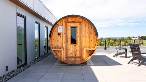 A wooden pod sits on a patio outside a modern building.