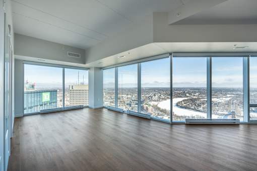 A large empty room with wooden floors and a view of the city through the windows.