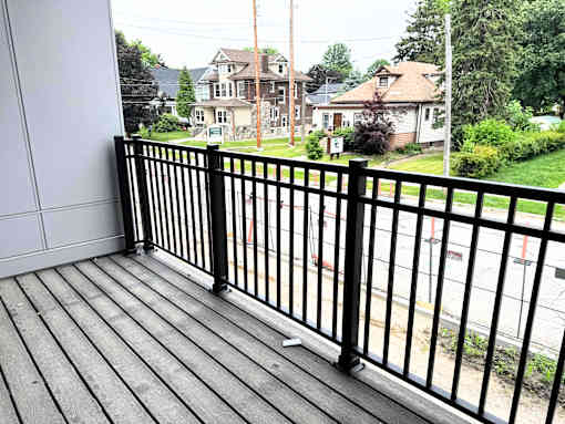 A black metal railing on a wooden deck overlooks a residential street.