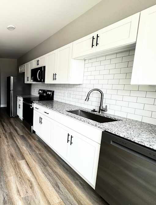 A kitchen with white cabinets and a black dishwasher.