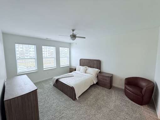 A bedroom with a bed, chair, and ceiling fan.