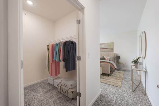 A bedroom with a bed, a nightstand, a chair, and a clothing rack with clothes hanging on it.