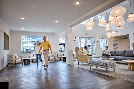 A man and woman are skateboarding in a spacious, well-lit room with modern furniture.