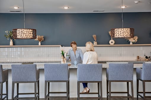 Two people sitting at a bar with grey chairs.