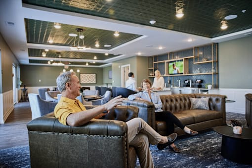 A man in a yellow shirt is sitting on a black leather couch.