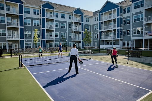 Two people playing tennis on a court with apartment buildings in the background.