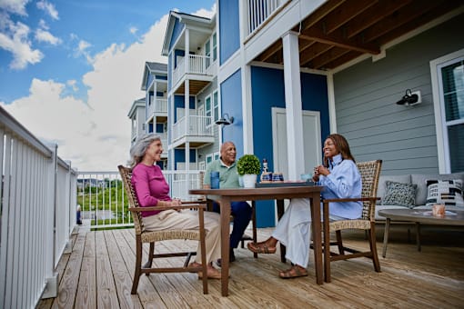 Three people are sitting at a table on a deck.