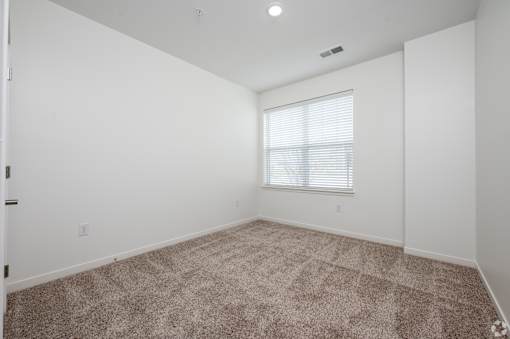 A room with a carpeted floor and a window with blinds.