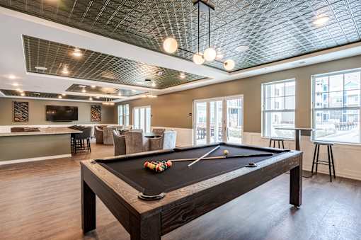 A pool table is in the middle of a room with a bar and a kitchen in the background.