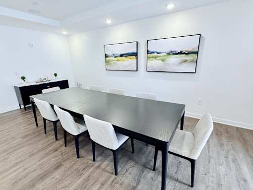 A long black table with white chairs in a room with two pictures on the wall.