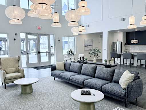 A grey couch with a white pillow is in the middle of a room with a grey carpet.