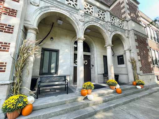 A building entrance with a bench and pumpkins on the steps.
