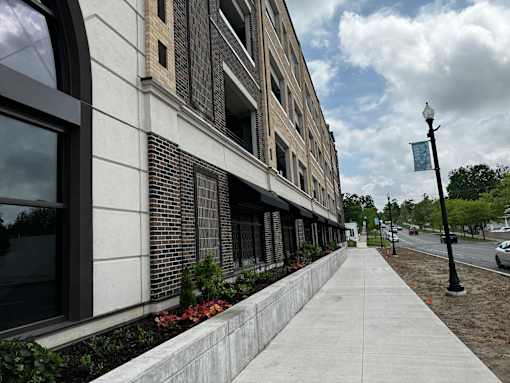 A sidewalk runs alongside a building with a brick facade and a street lamp.