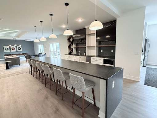 A modern kitchen with a long bar and chairs.